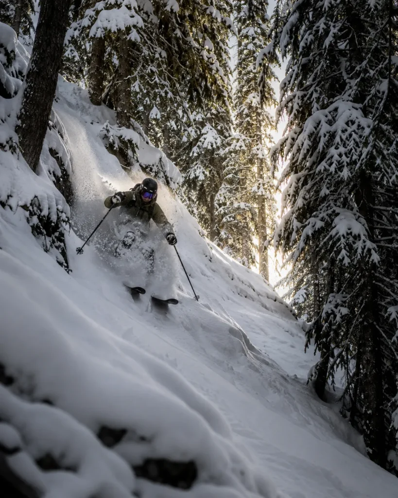 A skier dropping into a steep chute lined with snow-laden evergreens at Turner Mountain on a powder day