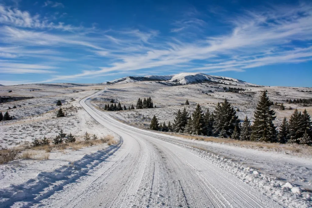 Snow-covered road winding through the rolling foothills of the Bears Paw Mountains in north-central Montana under a winter sky