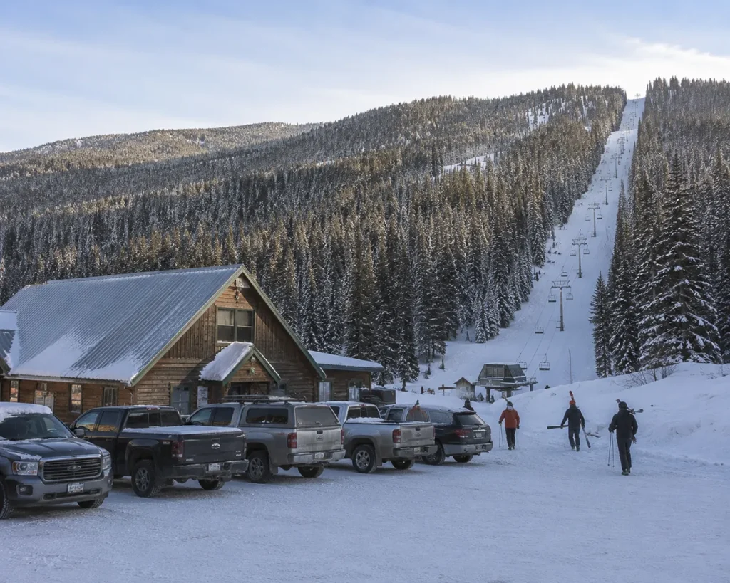 The base lodge at Turner Mountain Ski Area with a few cars parked and bundled-up skiers walking toward the chairlift on a snowy morning