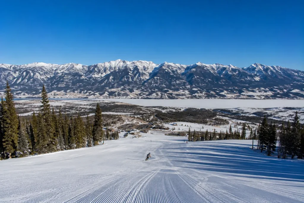 Empty wide-open ski run at Discovery Ski Area with the Flint Creek Range and Georgetown Lake visible in the distance under a clear blue Montana sky