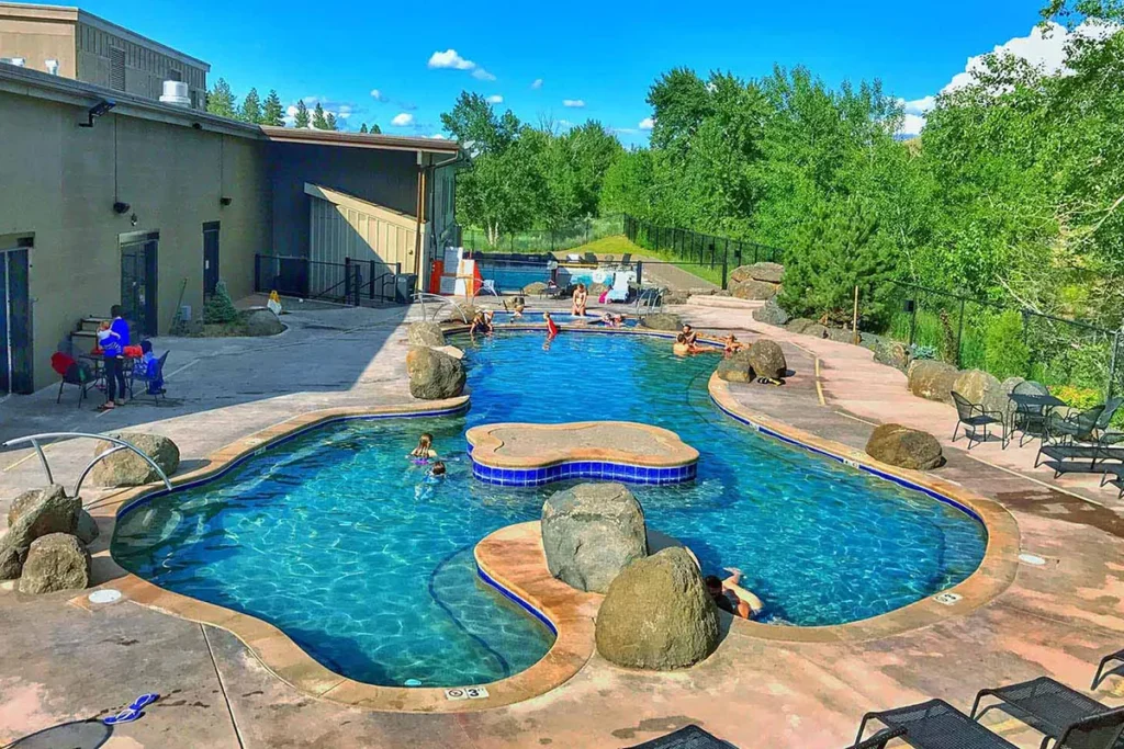Exterior view of Broadwater Hot Springs building with steam rising from outdoor pools and mountains in background