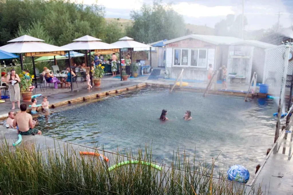 Overview of Norris Hot Springs wooden pool at dusk with steam rising and string lights visible