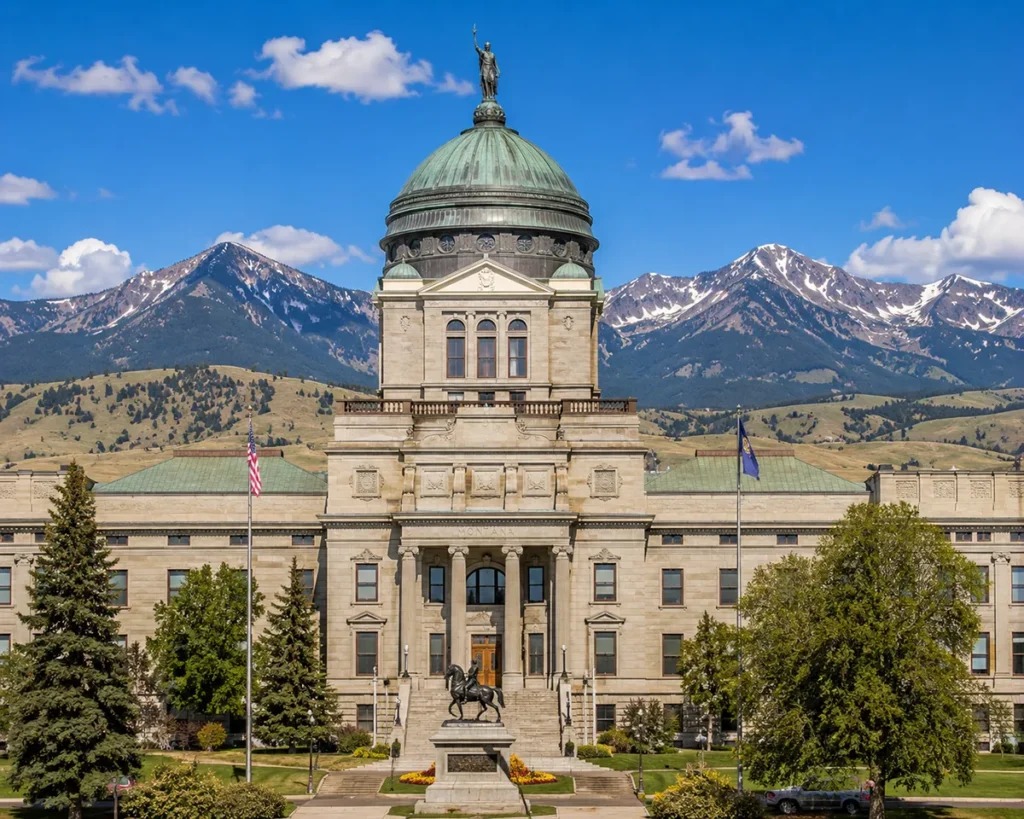Montana State Capitol Building exterior with copper dome against blue sky and mountain backdrop