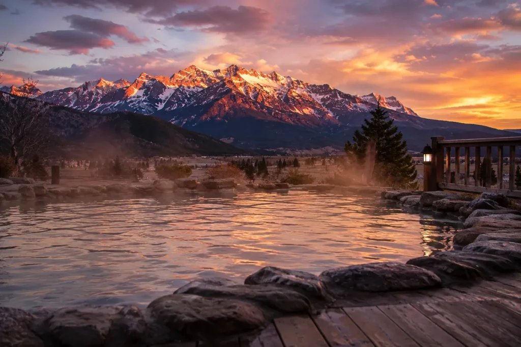 Person soaking in a Montana hot springs pool at sunset with mountains in background