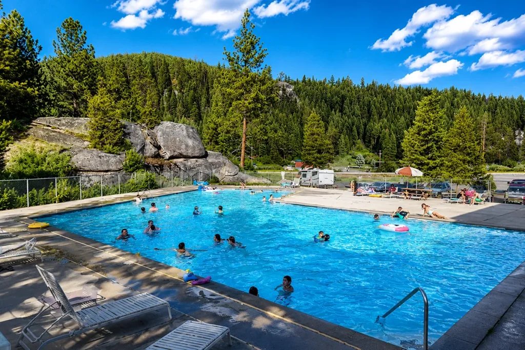 Aerial view of Lolo Hot Springs resort showing outdoor pool with steam rising, surrounded by evergreen forest and mountains