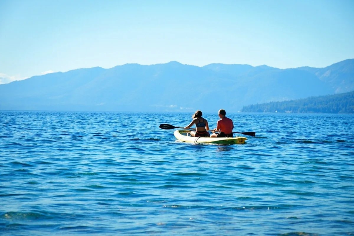 Clear blue water of Flathead Lake with mountain backdrop and family on paddleboard