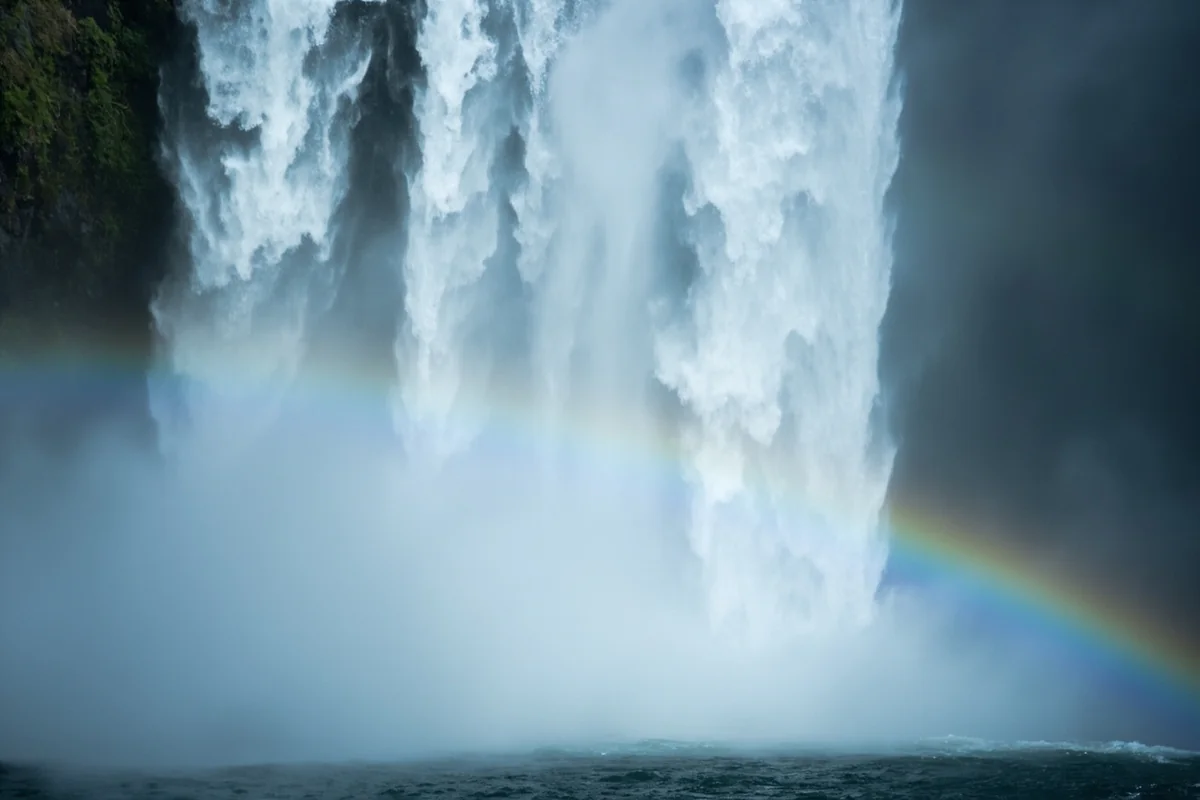 Close-up of waterfall mist creating rainbow effect with dark rock walls visible