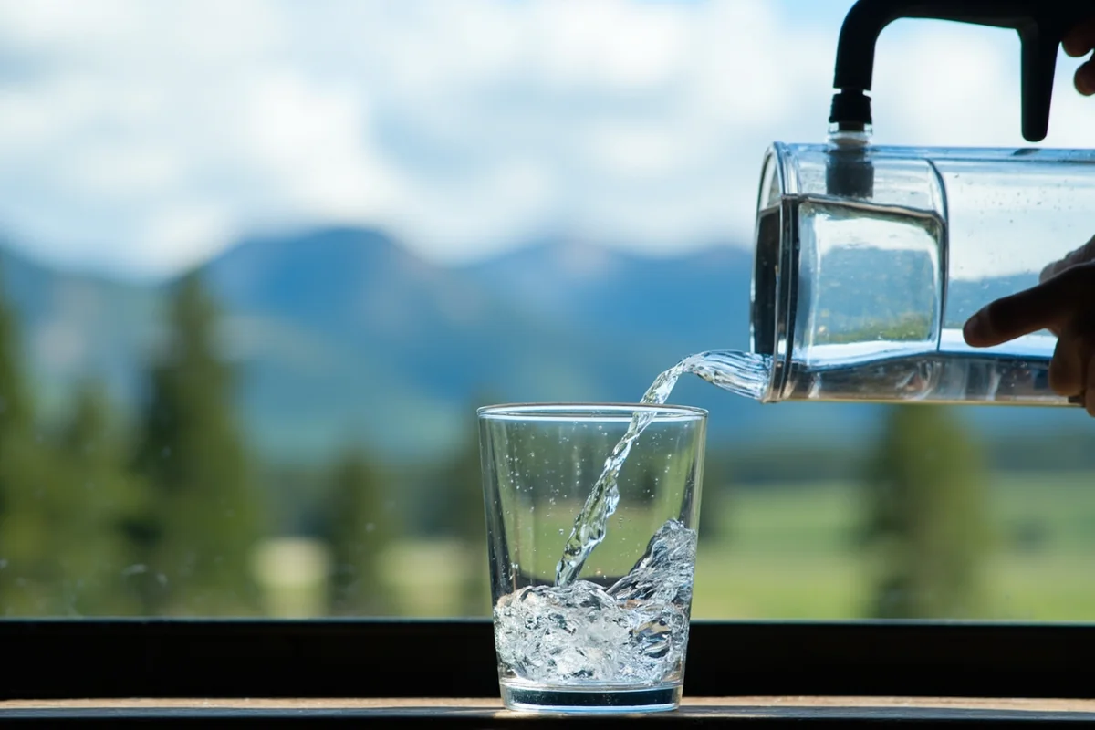 Crystal clear tap water being poured into a glass with Montana mountain backdrop through window