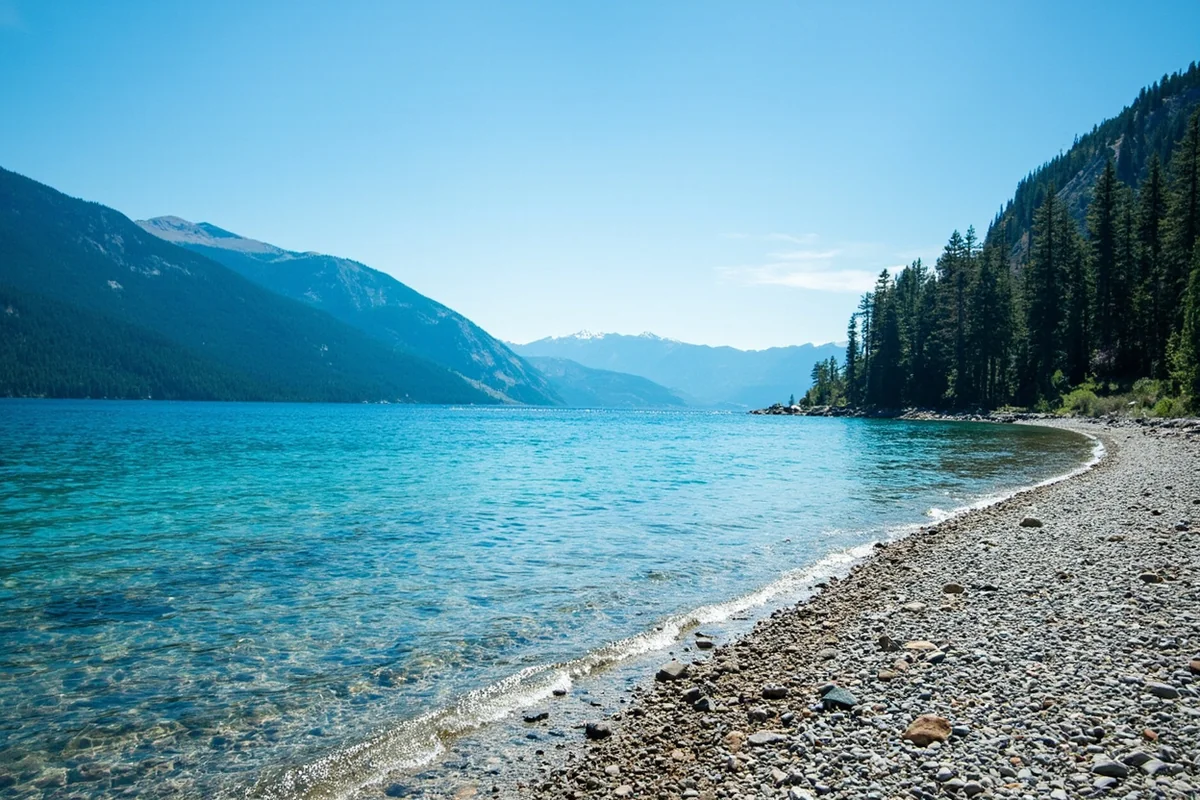 Crystal clear turquoise waters of Flathead Lake with pebble beach and surrounding mountains