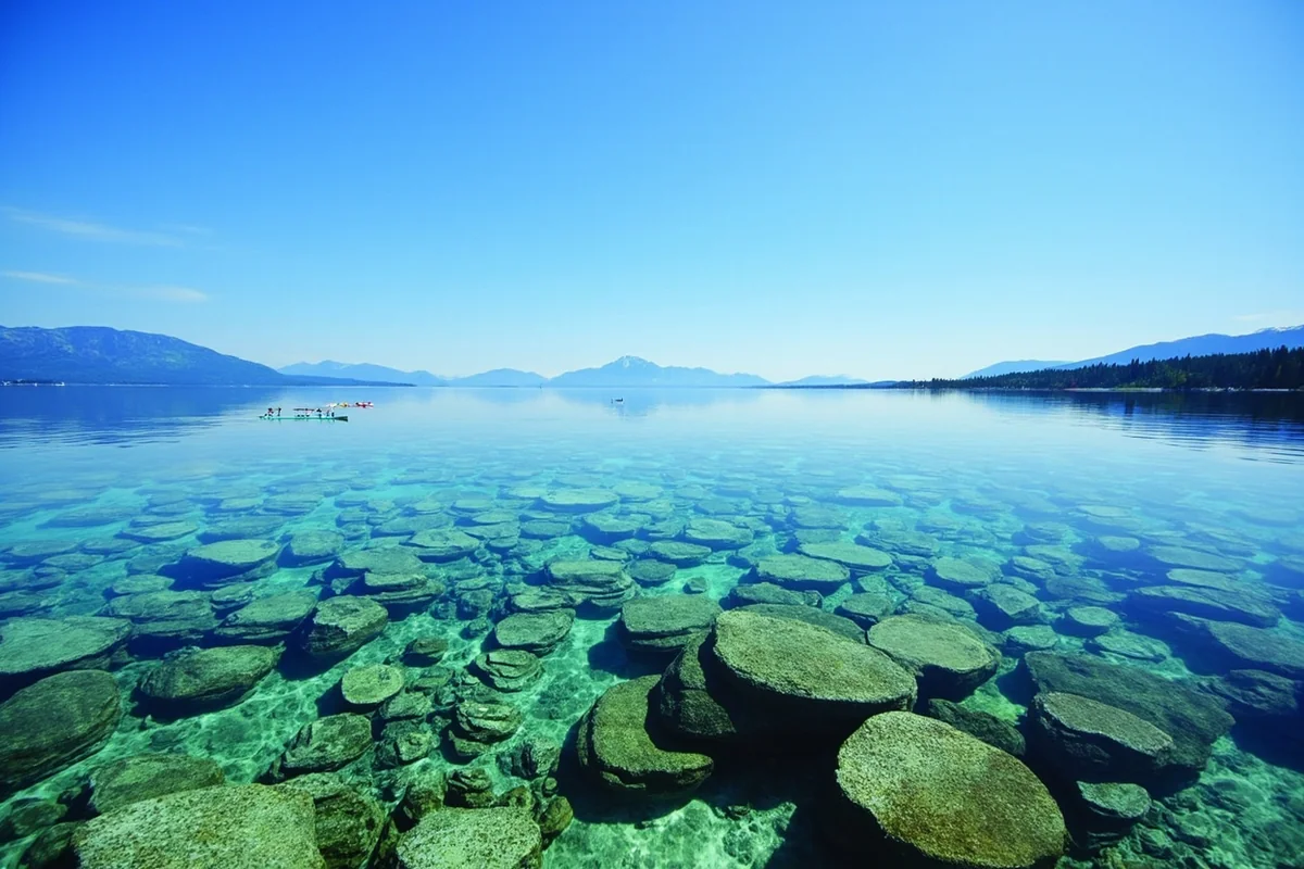 Crystal-clear waters of Flathead Lake showing visible rocks beneath the surface with a kayaker in the distance