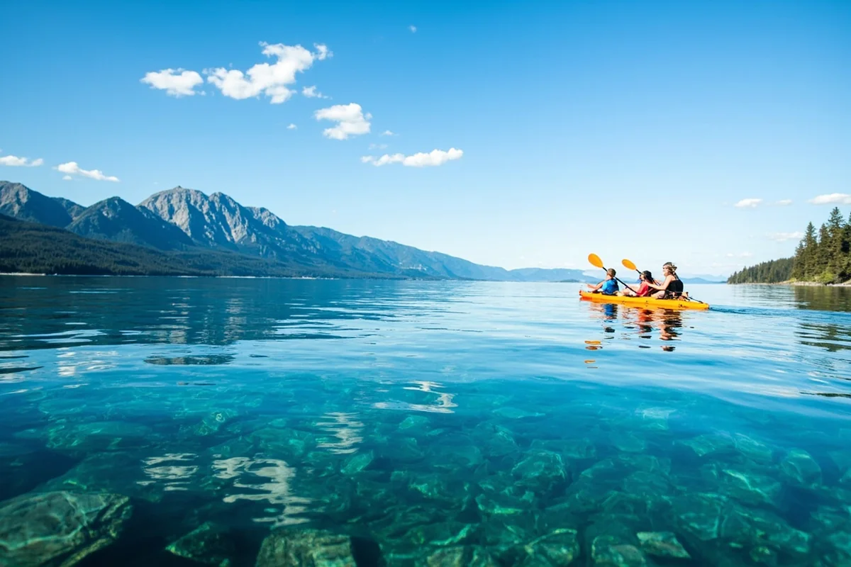Crystal clear waters of Flathead Lake with mountain backdrop and family kayaking in foreground