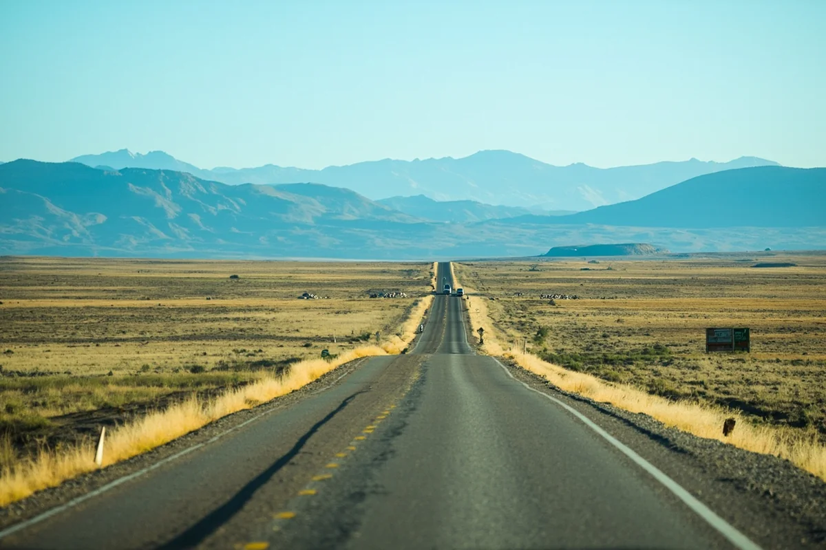 Empty two-lane highway stretching toward mountain horizon in central Montana with no other vehicles visible