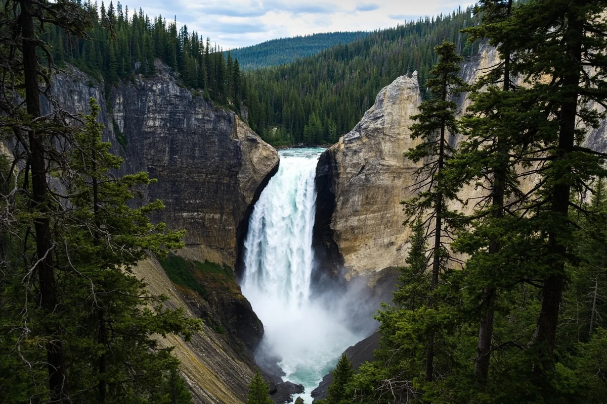 Hidden Falls cascading down rocky cliff face surrounded by dense forest in Glacier National Park