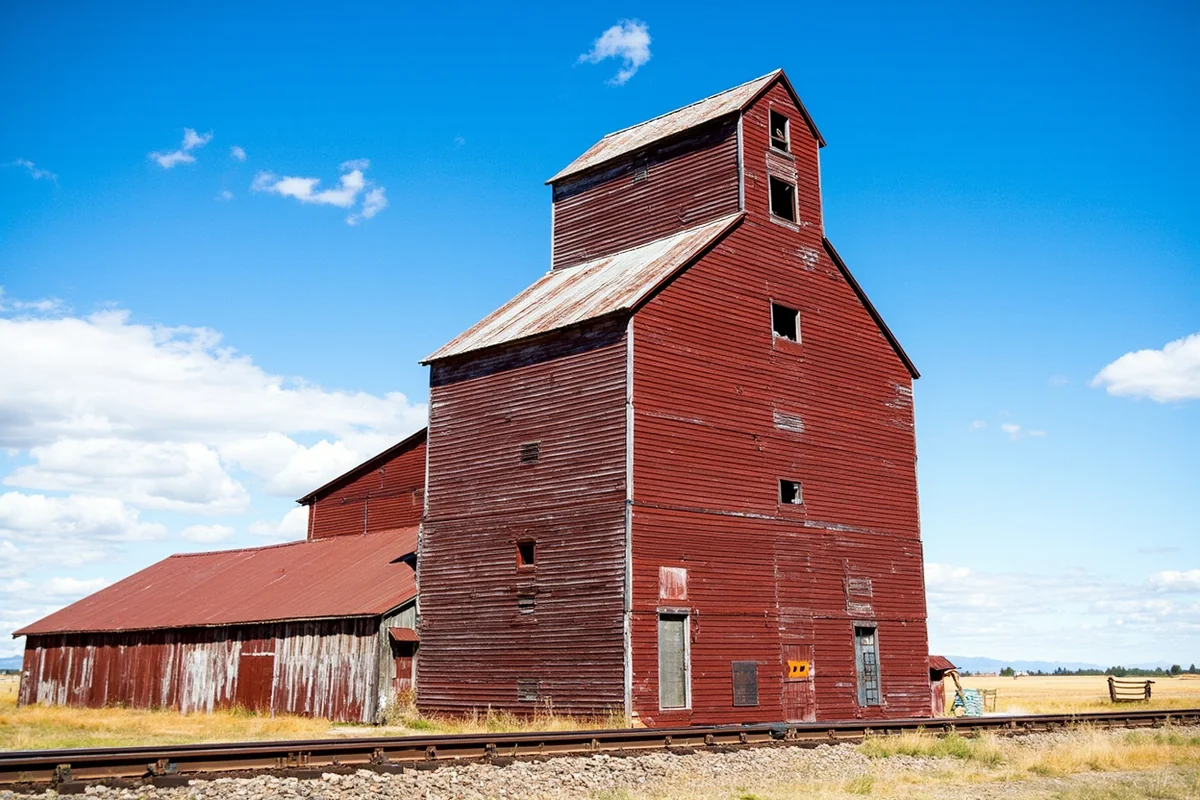 Historic wooden grain elevator against blue sky in Chester, Montana, showing weathered red paint and railroad tracks