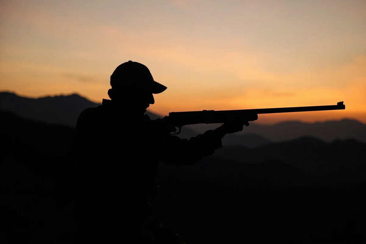 Hunter with muzzleloader rifle silhouetted against Montana mountain backdrop at dawn