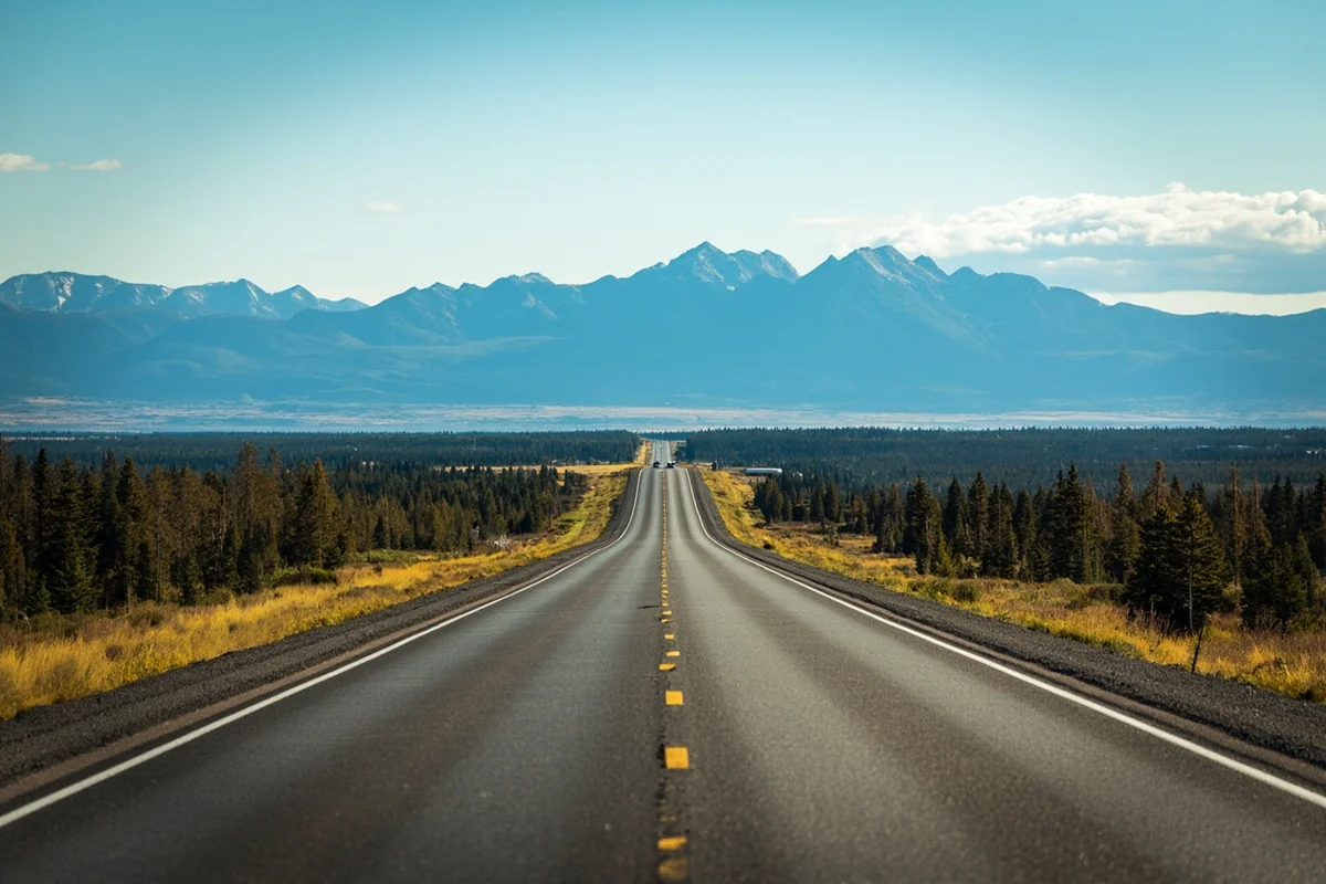 Long straight Montana highway stretching toward distant mountains, emphasizing the enormous distances