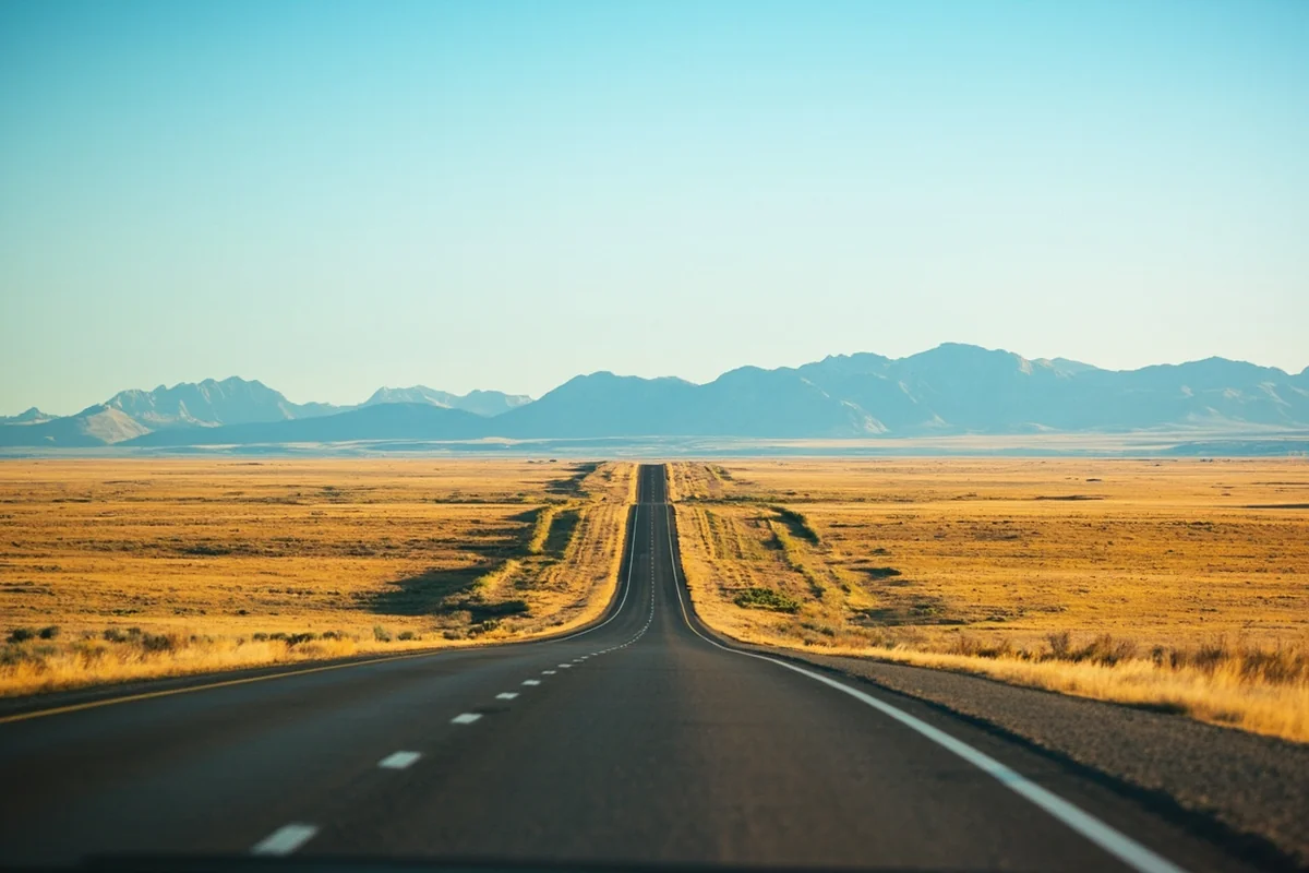 Long straight Montana highway stretching toward distant mountains with open prairie on both sides