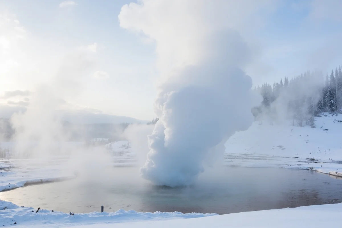 Old Faithful geyser erupting surrounded by winter snow and steam