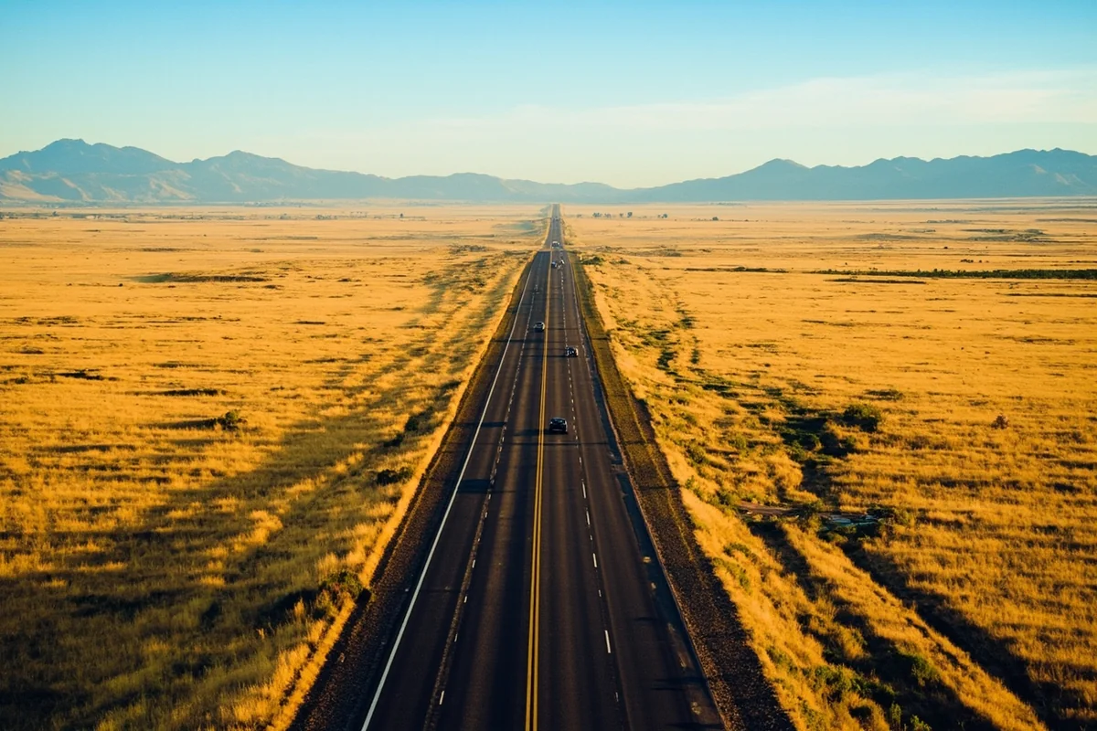 Overhead view of a Montana highway cutting through golden prairie grasslands with distant mountain ranges