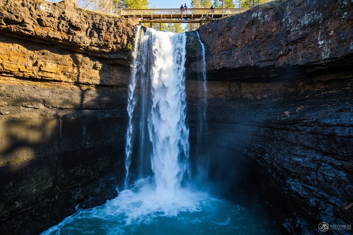 Palisade Falls cascading down volcanic rock cliff face with hikers at viewing platform