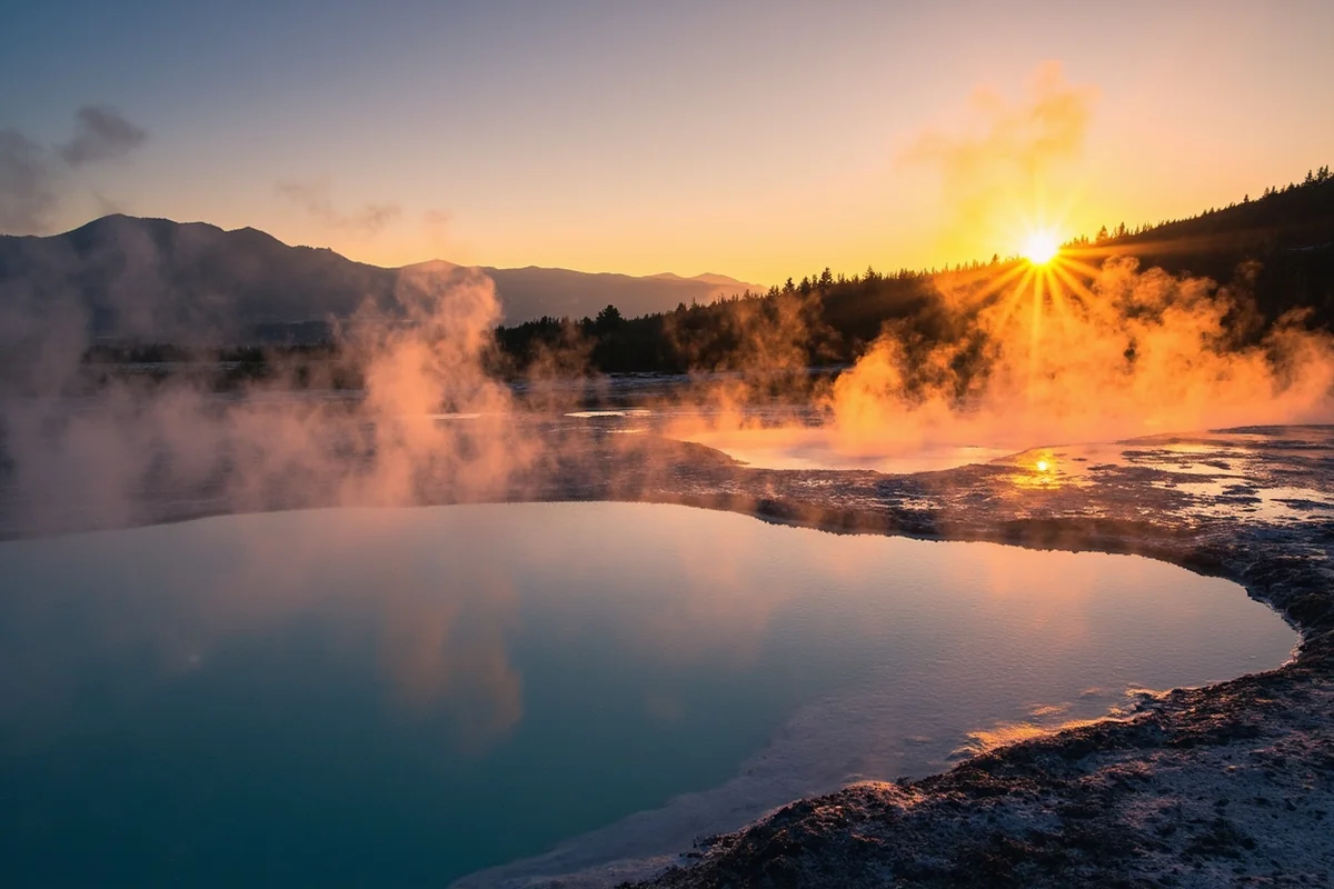Panoramic view of steam rising from a Montana hot spring with mountain backdrop at sunset