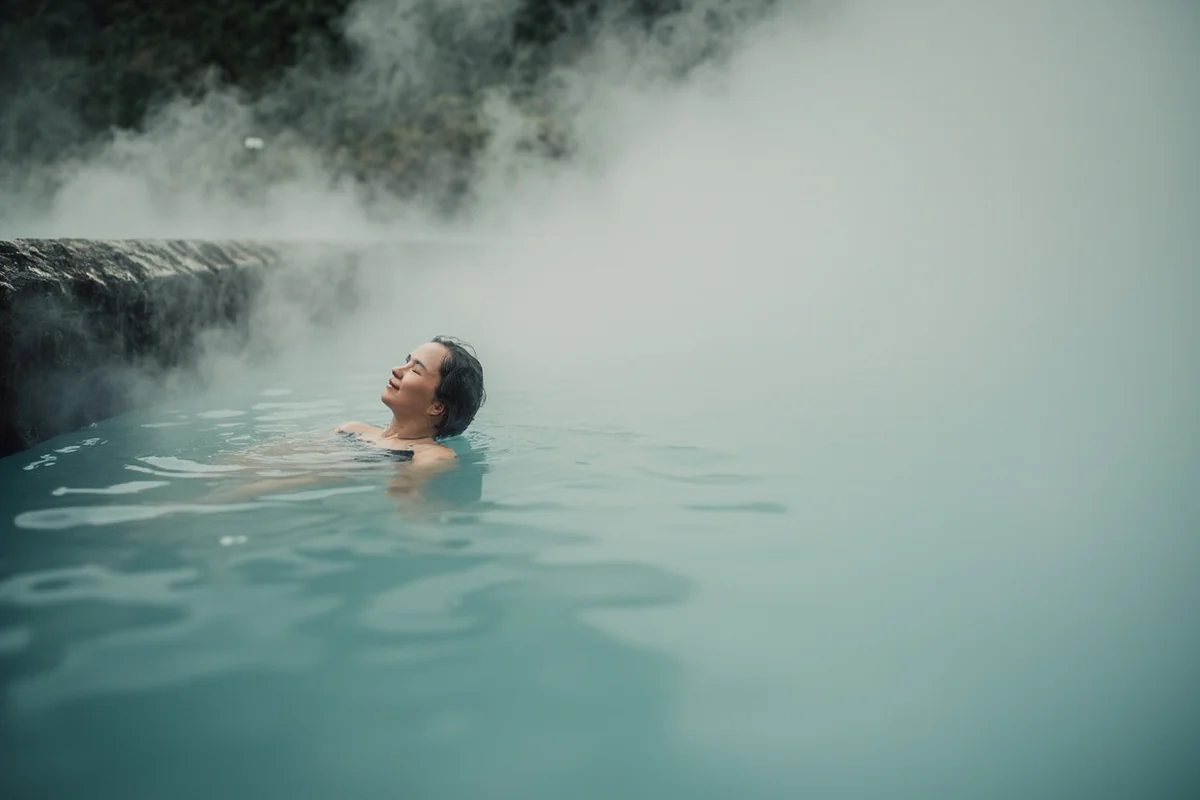 Person relaxing in natural hot spring with steam rising around them