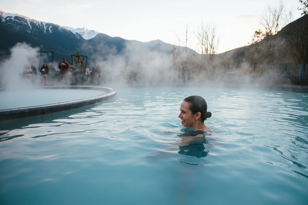 Person relaxing in outdoor pool at Lolo Hot Springs with mountain views and steam rising