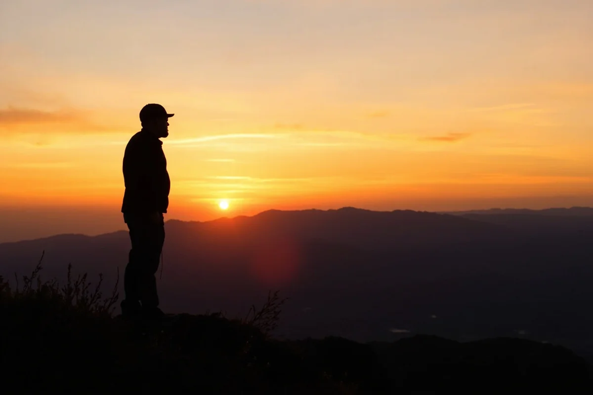 Person standing on mountain overlook watching sunset