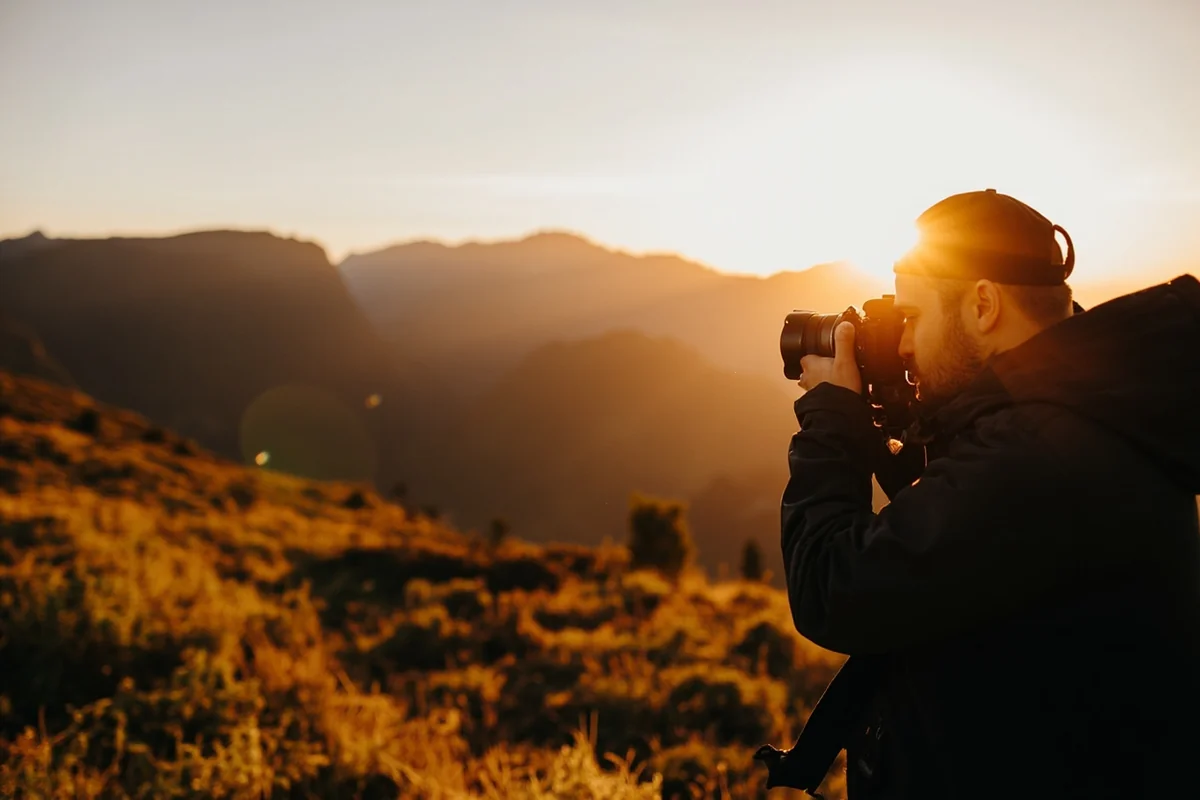Photographer at dawn with mountains and meadow in background