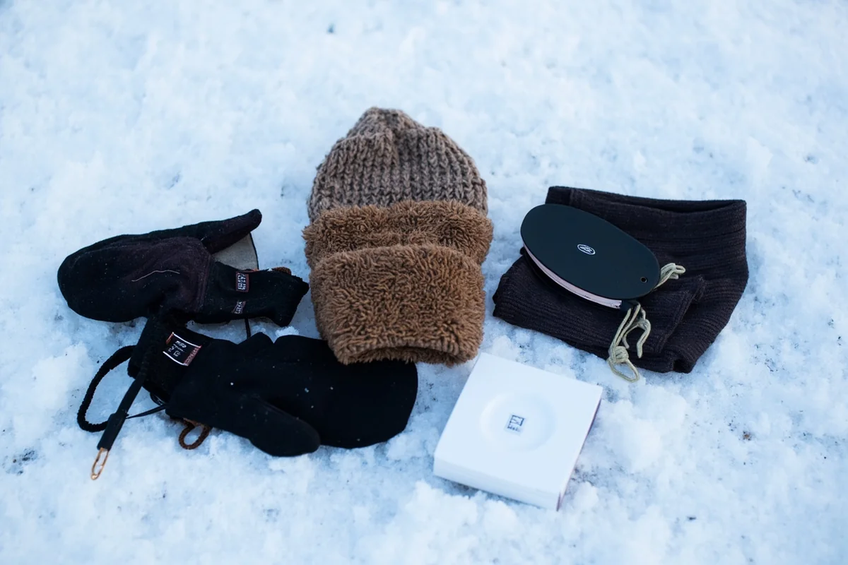 Proper winter accessories laid out - mittens, balaclava, warm hat, and neck gaiter on snowy surface