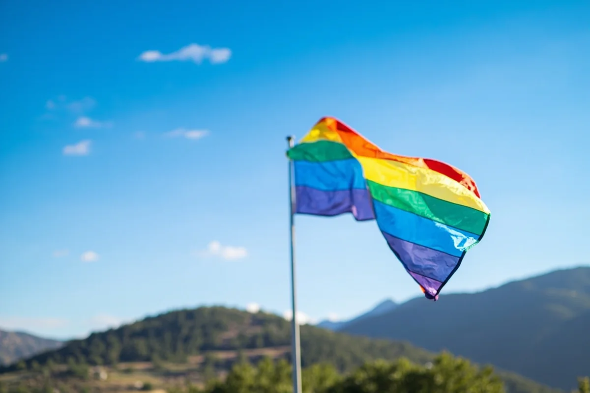Rainbow flag flying against Montana mountain backdrop with blue sky