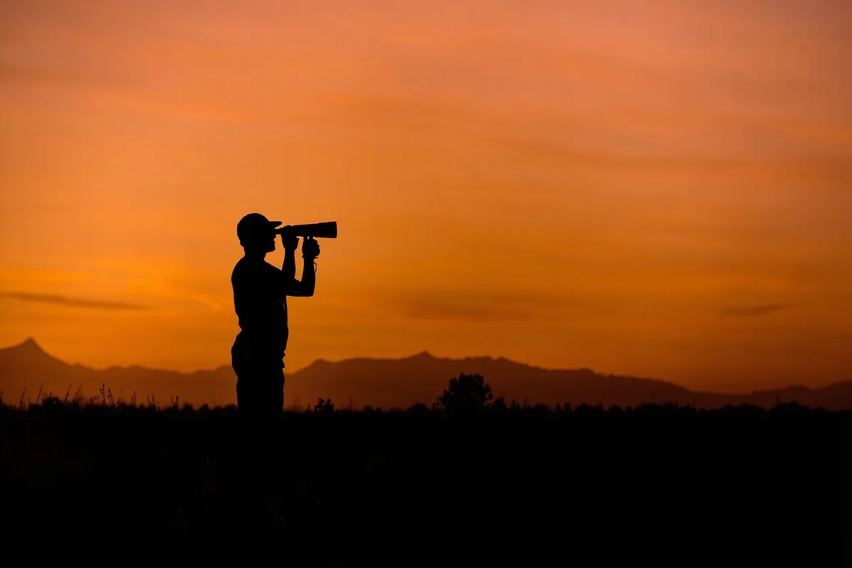 Silhouette of birder with binoculars against Montana sunset with mountain range