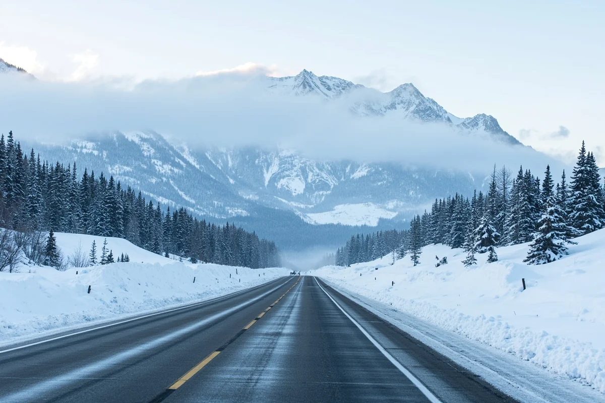 Snow-covered Montana highway with mountain backdrop during winter, showing cleared road with snow banks on both sides