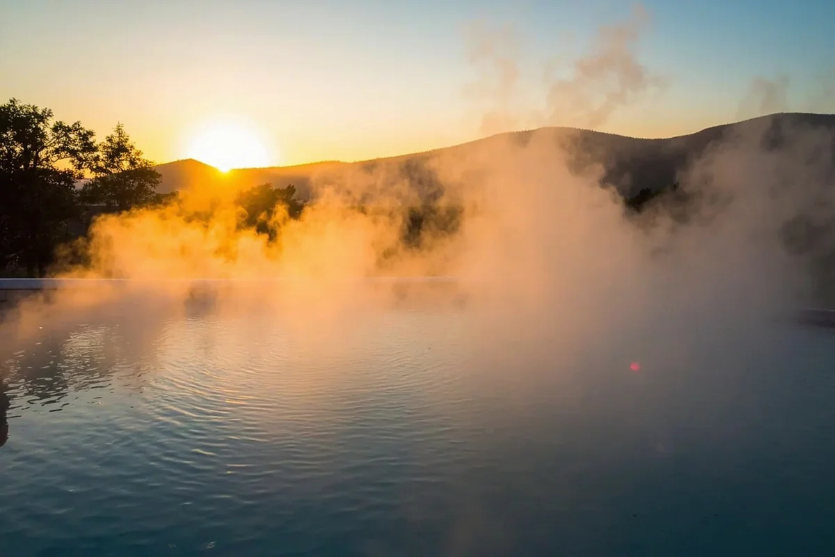 Steam rising from a natural hot spring pool with mountain backdrop at sunset