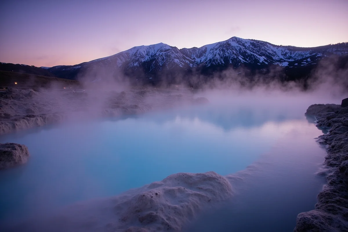 Steam rising from Chico Hot Springs pool at dusk with snow-covered mountains in the background