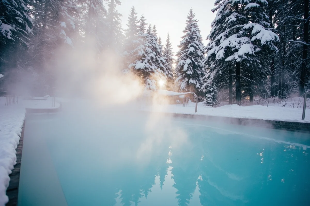 Steam rising from hot springs pool during winter snowfall at Quinn's Resort