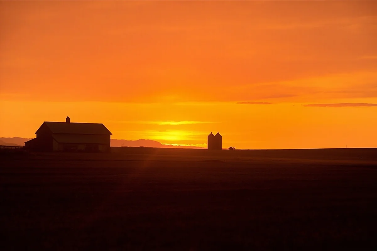 Sunset over Montana farmland with silhouetted barn and grain silos