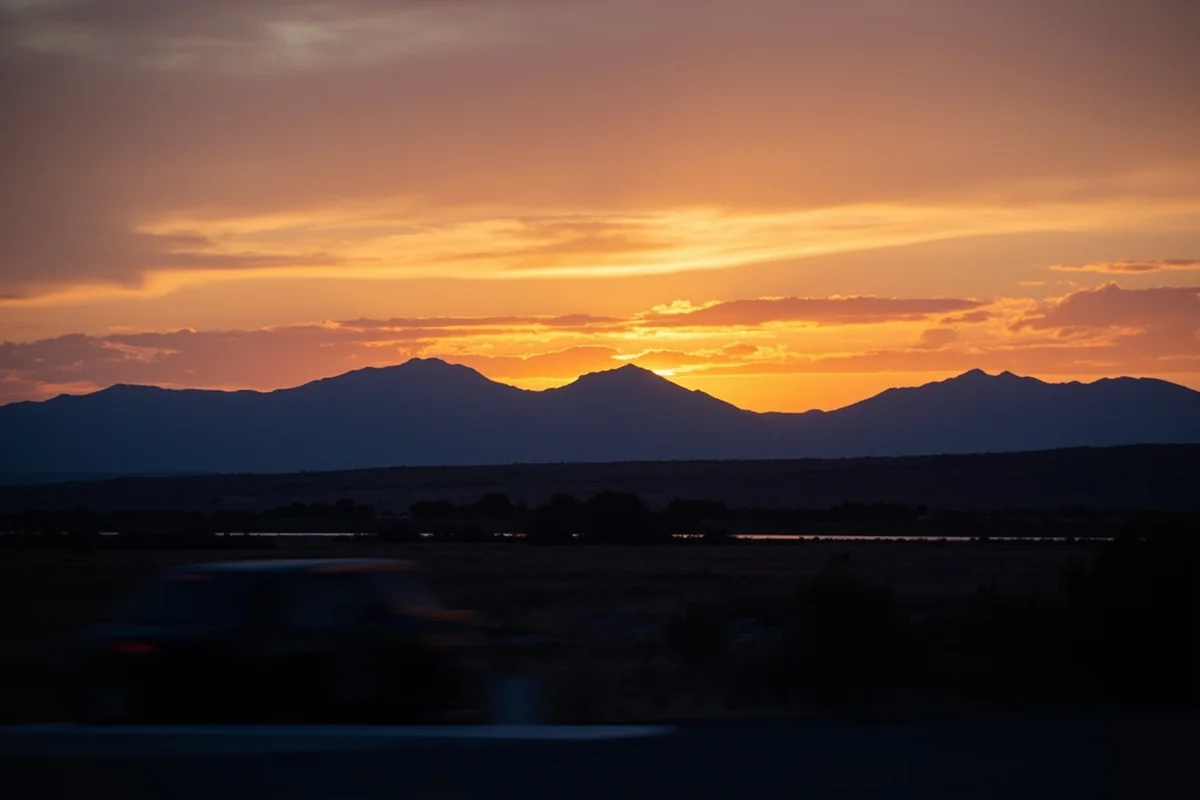 Sunset over Montana mountain range viewed from highway pullout, car visible in foreground