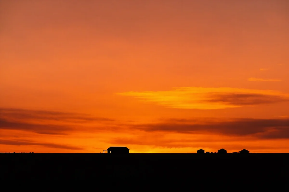 Sunset over Montana prairie with silhouette of lone ranch buildings