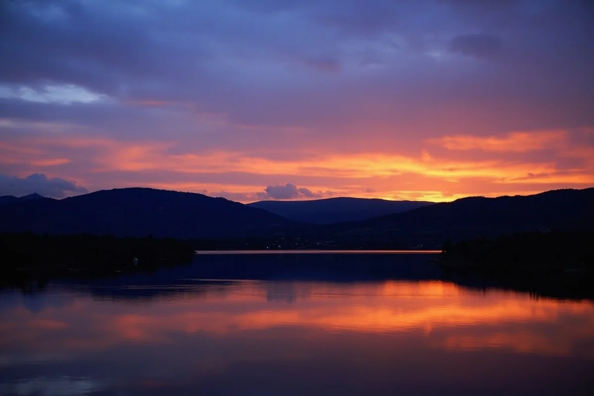 Sunset view from Two Medicine Lake area with silhouetted mountains and calm water reflection