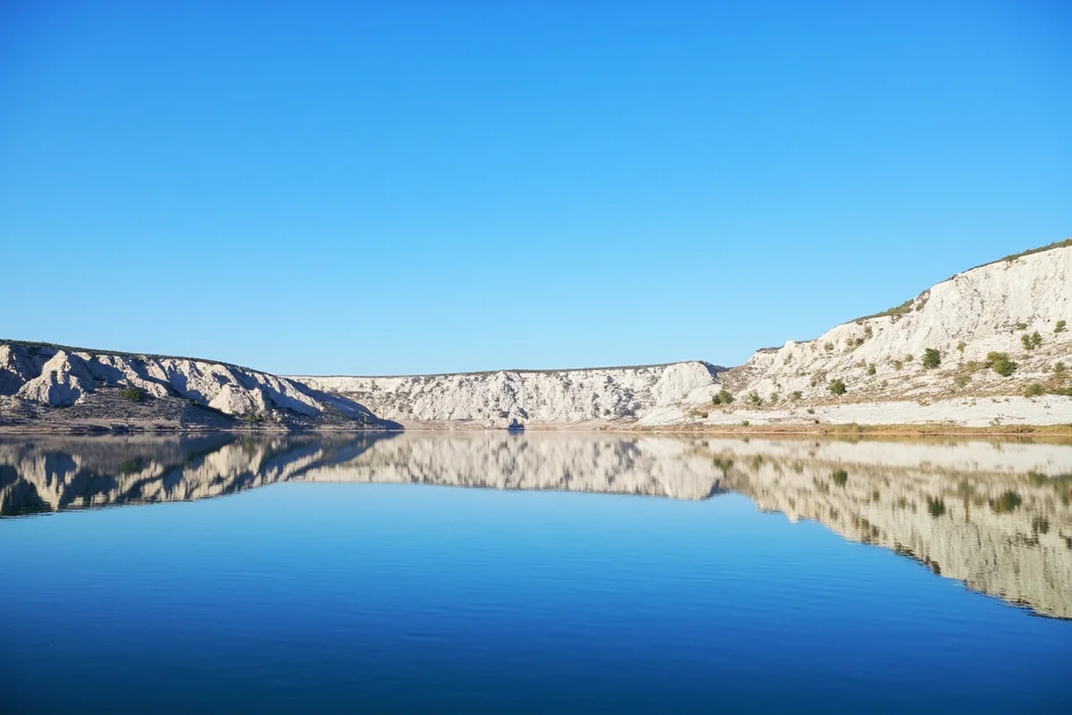 White sandstone cliffs along Missouri River with blue sky reflection on calm water