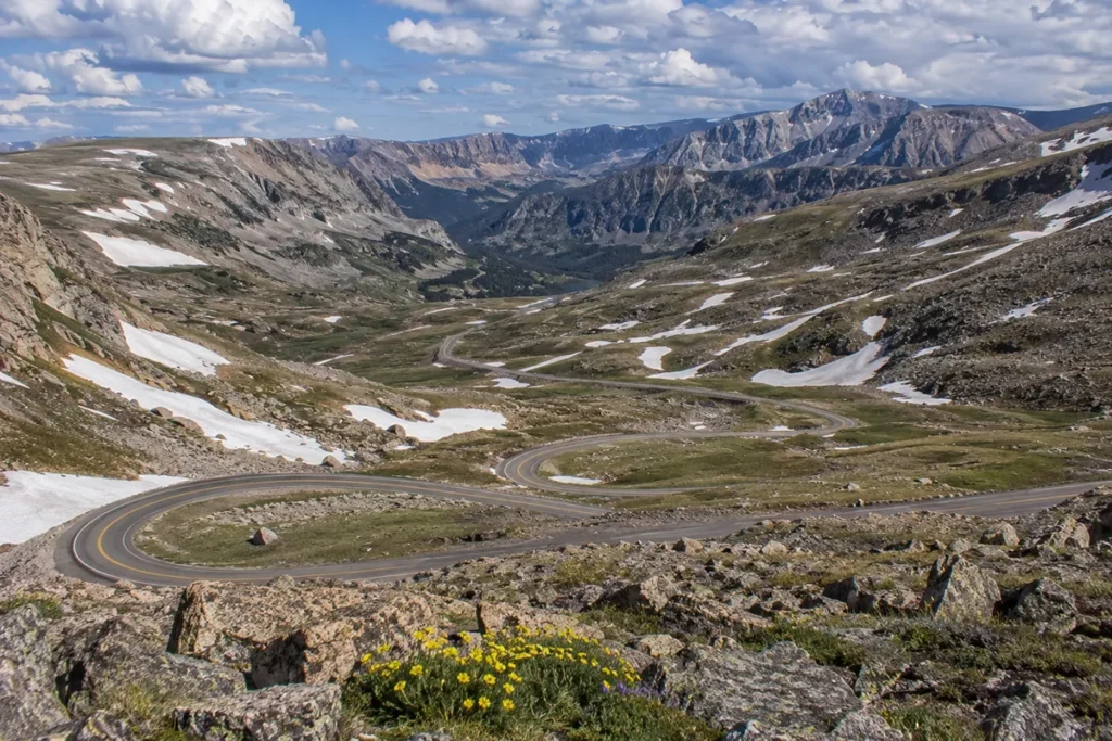 The famous switchbacks of the Beartooth Highway climbing through alpine tundra above 10,000 feet with patches of snow visible on the surrounding mountains in June