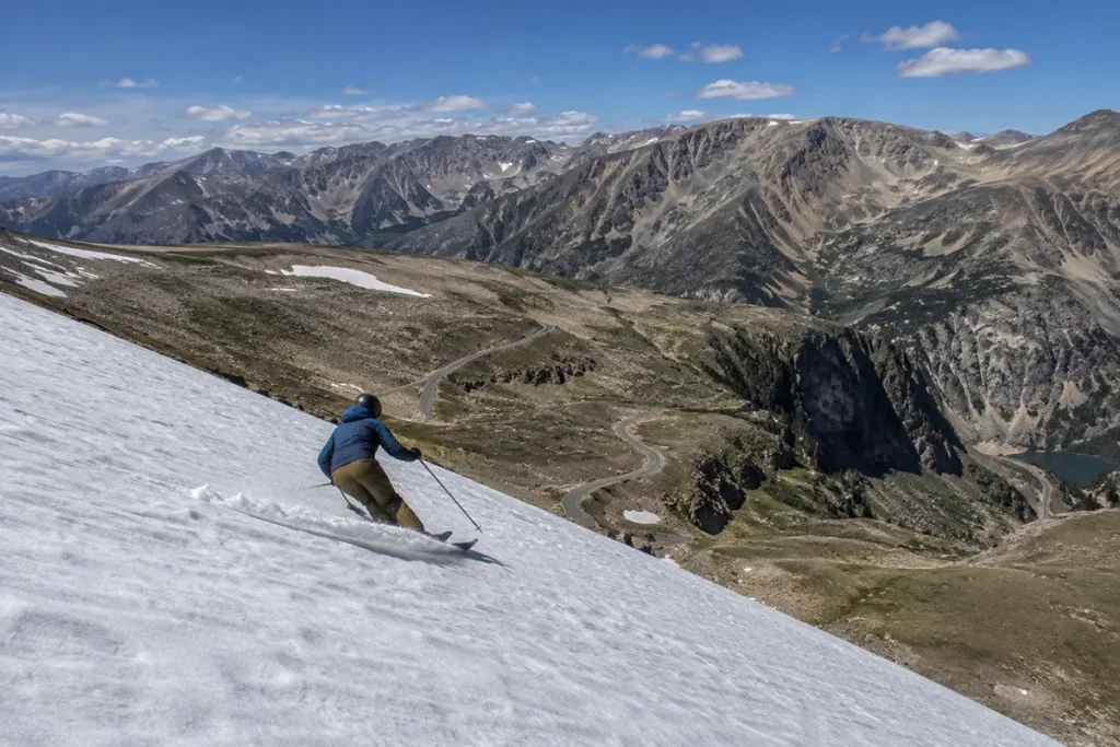 A skier carving down the Twin Lakes Headwall at Beartooth Basin in summer with the surrounding mountains bare of snow and the Beartooth Highway visible far below