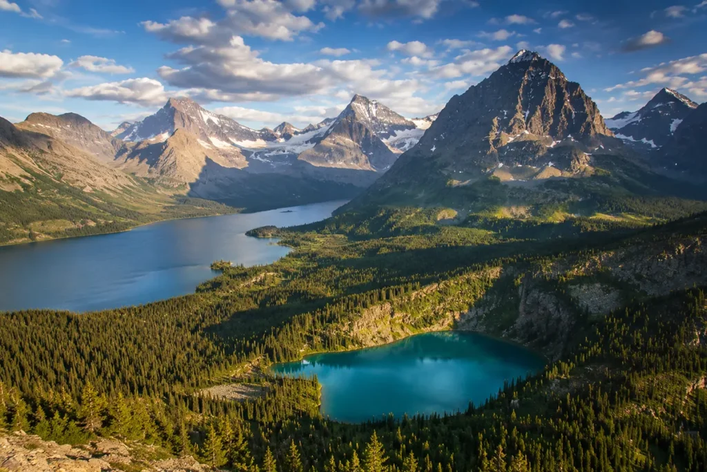 Aerial view of Glacier National Park's Many Glacier valley showing turquoise alpine lakes, dramatic mountain peaks, and pine forests in late summer