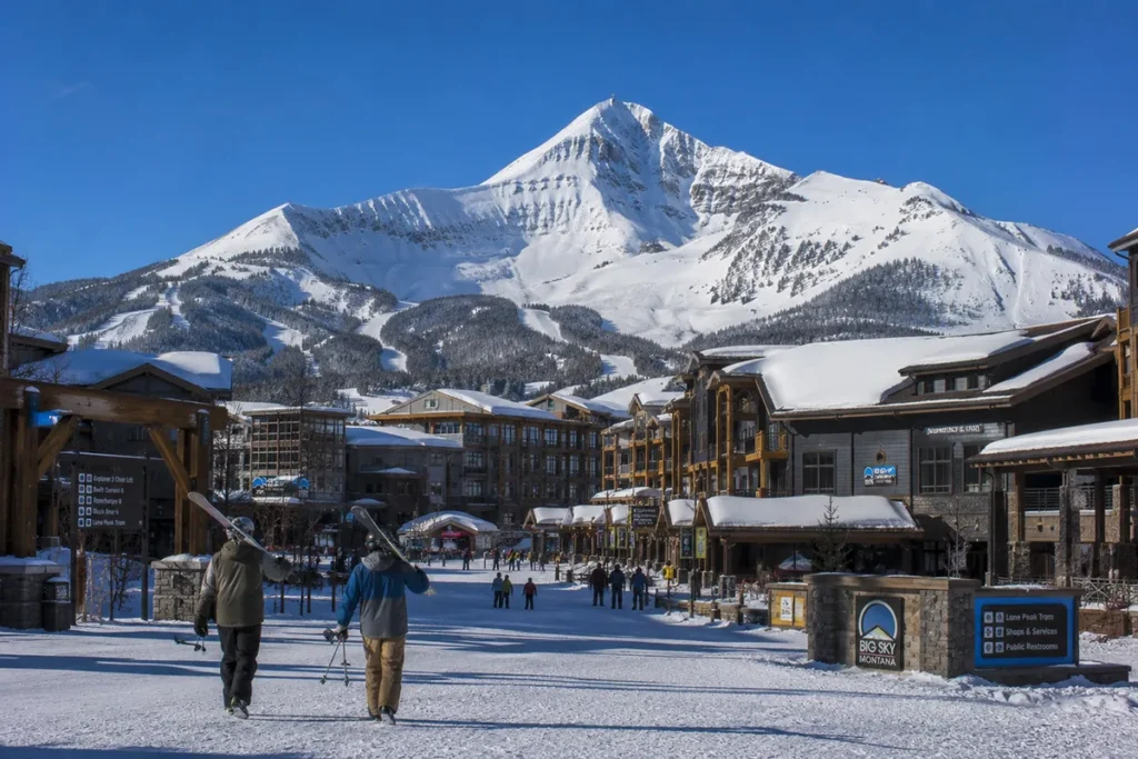 View across the Big Sky Mountain Village base area with modern hotels and lodges in the foreground and Lone Peak rising dramatically in the background