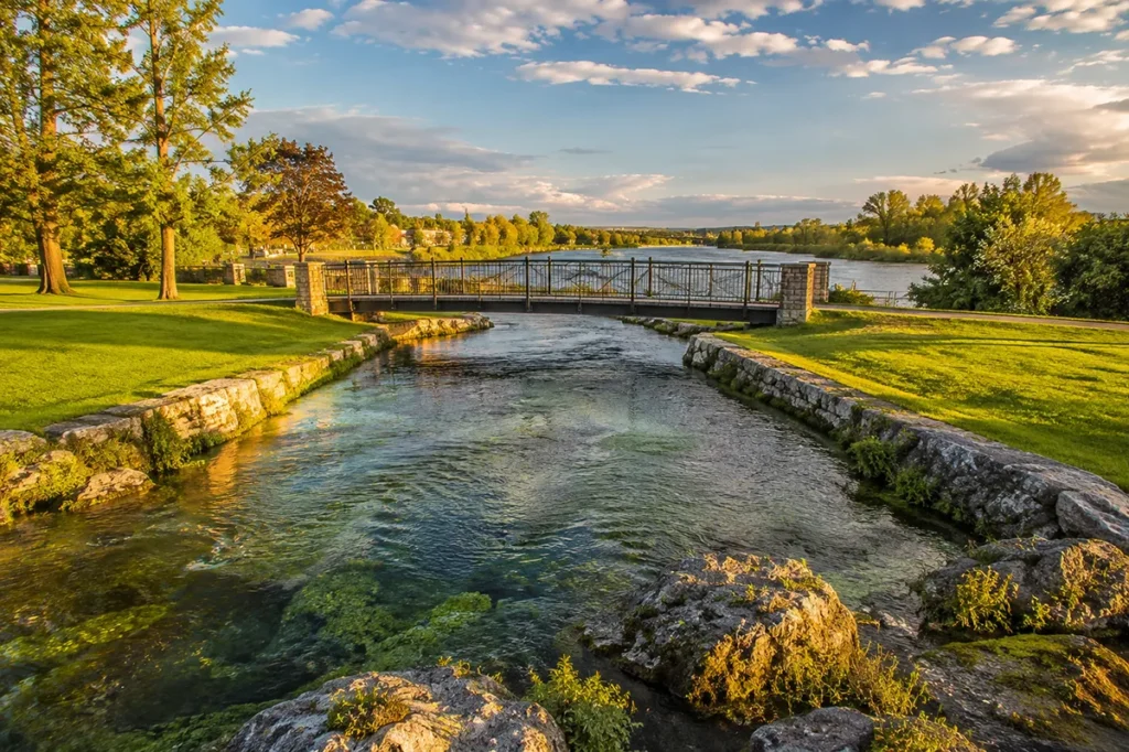 The Roe River flowing from Giant Springs into the Missouri River, with the viewing bridge and surrounding park visible at Giant Springs State Park, Great Falls