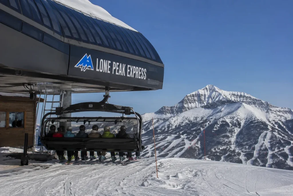 The Madison 8 high-speed chairlift at Big Sky Resort loading skiers under a clear winter sky with Lone Peak in the background