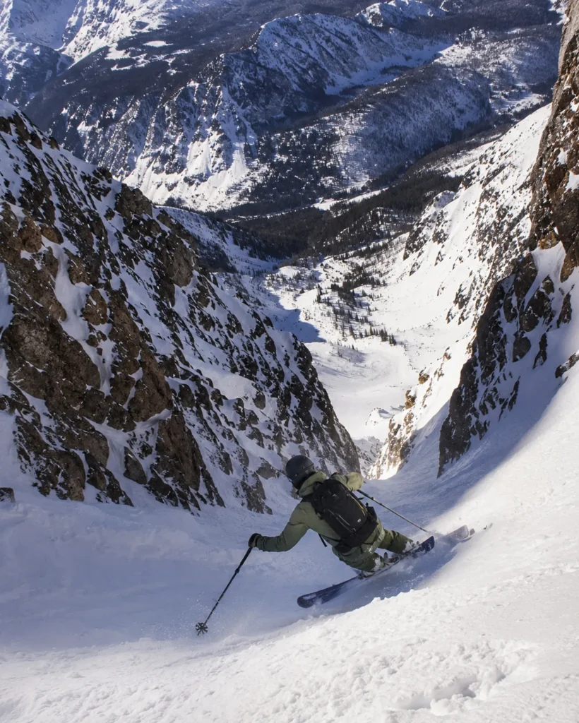 A skier descending the steep Headwaters terrain at the Moonlight Basin side of Big Sky with dramatic chutes and exposed cliff bands visible