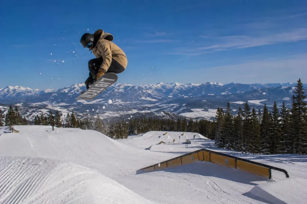A snowboarder catching air off a jump in one of the Great Divide terrain parks with multiple features visible behind