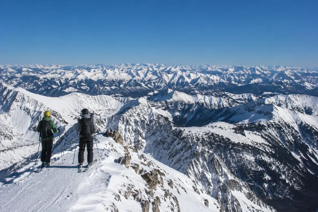 View from the summit of Lone Peak at Big Sky Resort looking out across the Madison Range to the Spanish Peaks with skiers visible at the top of the tram
